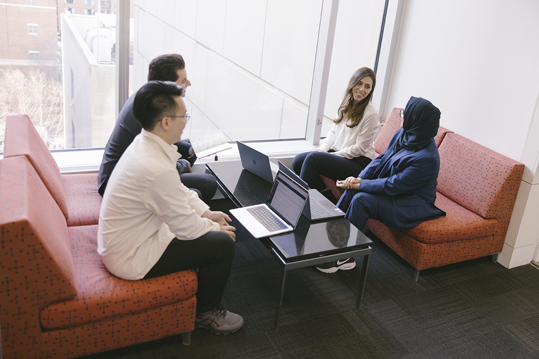 Four GWSB information systems technology students chat at a table in front of a large window in Duques Hall