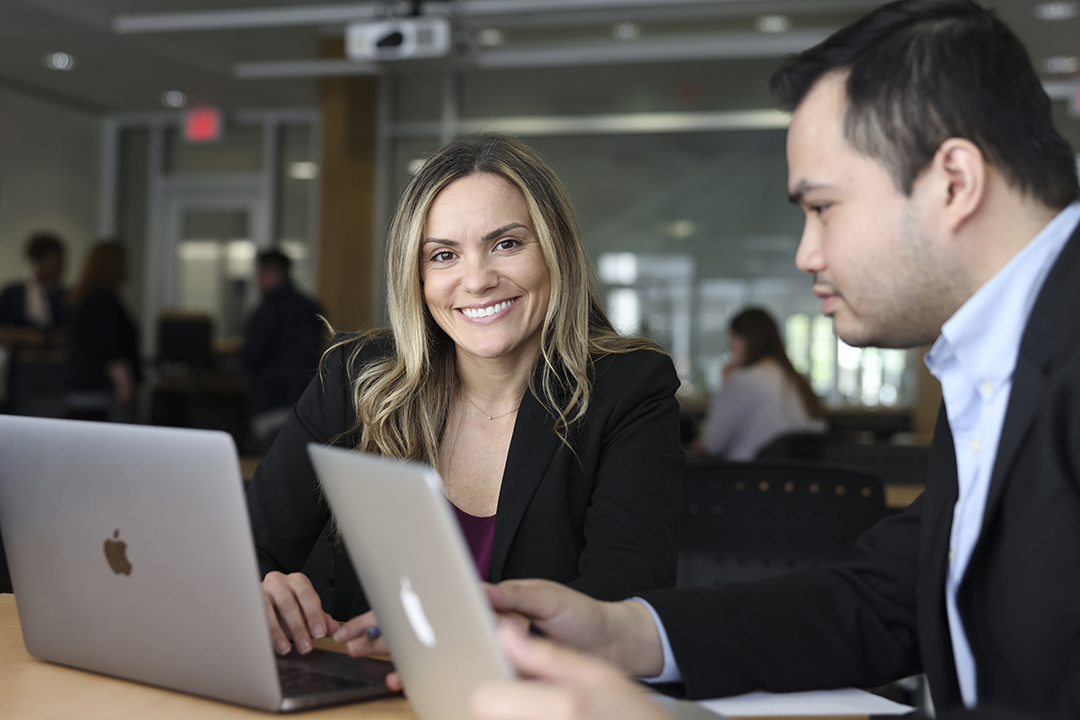 Two GWSB Global MBA students work at laptops at a shared table outside of a classroom