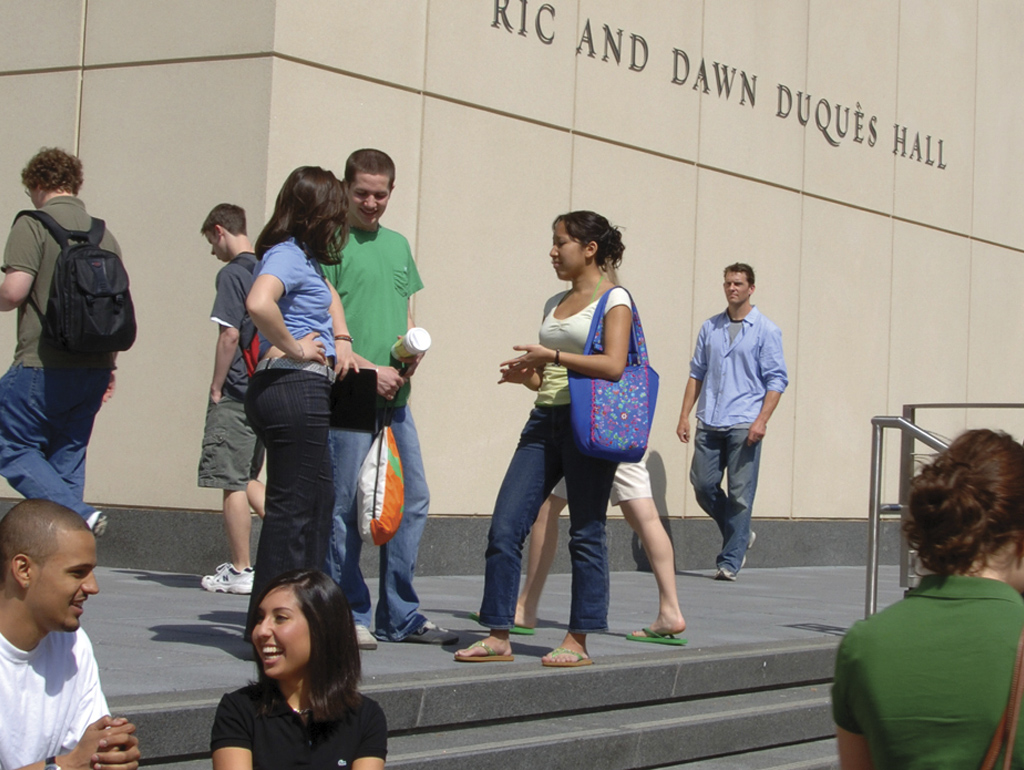 students gather on a sunny day in front of Duquès Hall, the home of the GW School of Business
